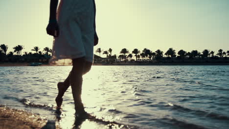 Unknown-girl-walking-in-warm-seawater-in-sunrise.-Woman-legs-splashing-water