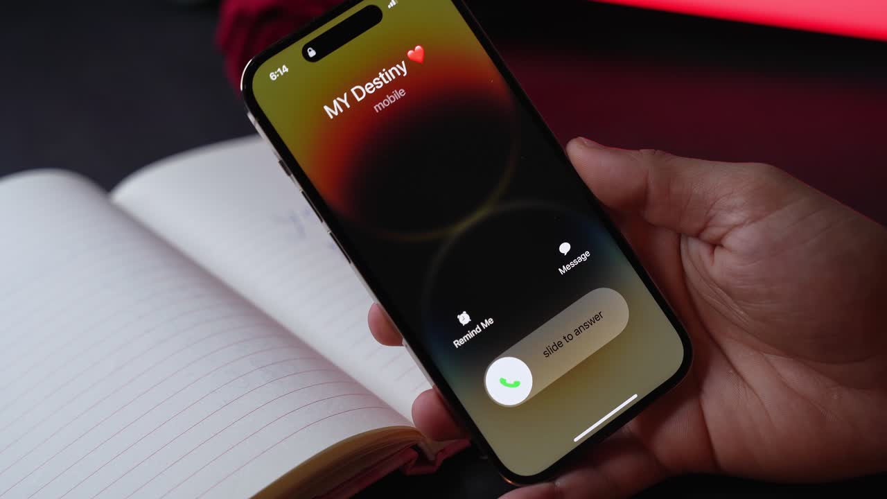 Close-up of hand holding smartphone with incoming call over open lined notebook, moody red low light and blurred rose background, romantic communication and relationship tension concept