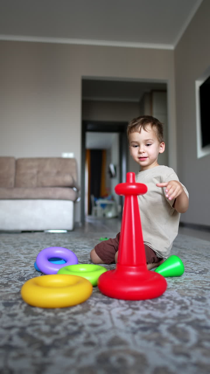 Lovely smiling Caucasian toddler playing cheerfully at home. Little kid builds a pyramid. Vertical video.