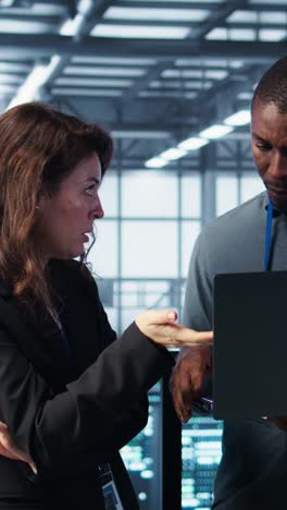 Vertical video Developers in data center workspace coding on laptop, analyzing metrics