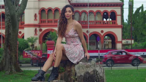 young pretty latina sits on a log at thr park with a castle in thee background in the capital city of trinidad and tobago