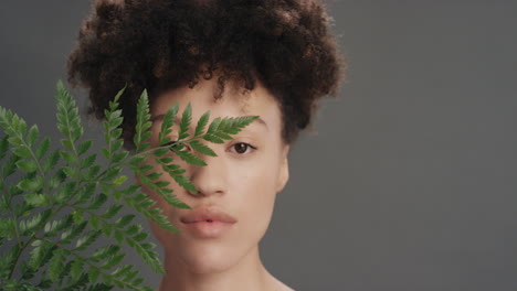 retrato de una hermosa mujer de raza mixta tocando la cara con una hoja acariciando una piel suave y saludable disfrutando de una belleza natural juguetona sobre un fondo gris