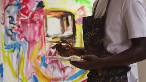 mid section of african american male artist wearing apron painting on canvas at art studio