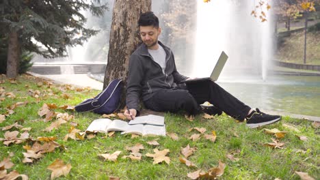 Young-adult-male-student-studying-in-nature-in-park-on-grass-using-laptop.