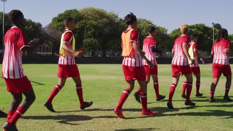 video of diverse group of male football players warming up on field, running and stretching