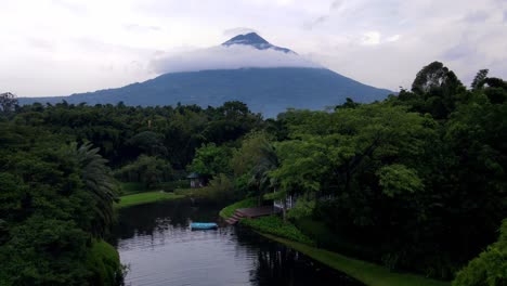 volando sobre un estanque con un puente y una fuente en antigua, guatemala, acercándose al impresionante volcán en el cielo