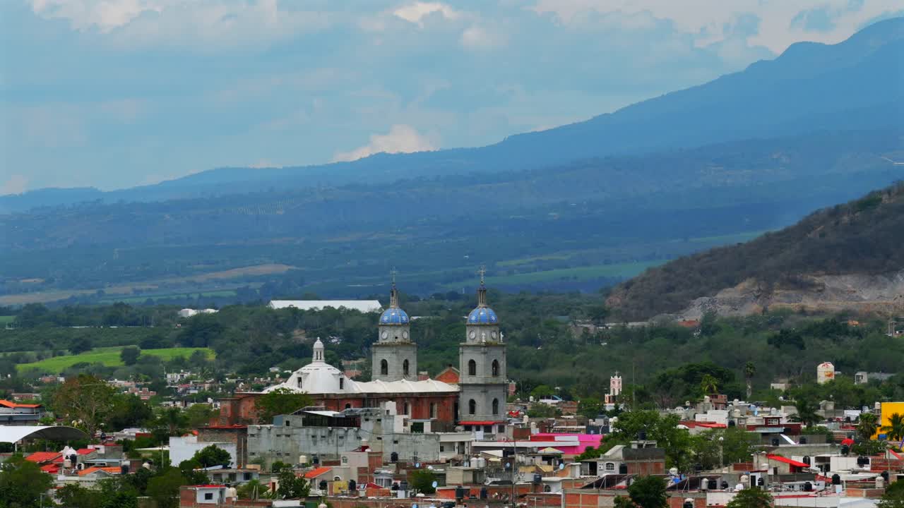 Daytime panoramic side view of San Juan de Bautista church in Tuxpan Jalisco surrounded by mountains and Colima volcano range