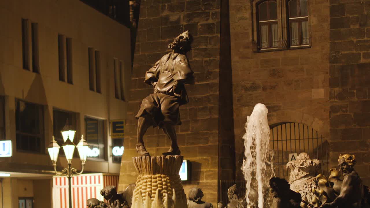 Corn statue and fountain illuminated at night, gentle water movement, stationary camera, urban setting