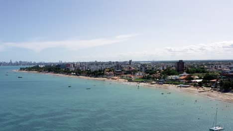 aumento de camiones a la derecha vista aérea extrema de la playa tropical de bessa en la ciudad capital de joao pessoa, paraiba, brasil con gente disfrutando del océano rodeada de palmeras y edificios