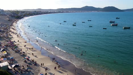 Aerial-drone-view-of-tropical-beach-with-many-people-enjoying-the-sand-and-sea-in-late-afternoon