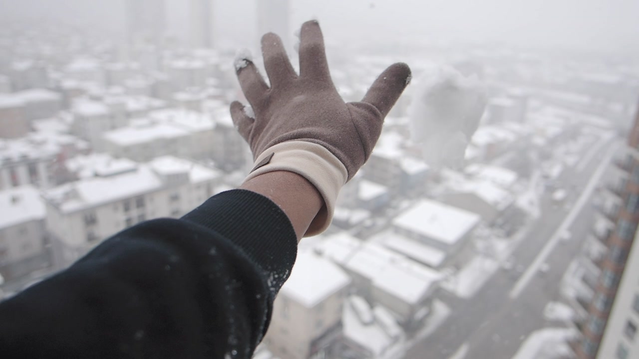 Gloved Hand Releasing Snow Over a Snowy Cityscape