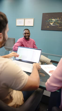 vertical video: collaborating in office, colleagues using laptop and documents while discussing proj