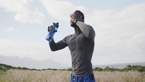 Hombre-Afroamericano-Vertiendo-Agua-En-Su-Cara-Mientras-Hace-Ejercicio-En-El-Campo