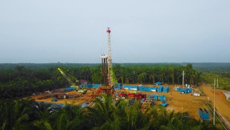 Cinematic-Drone-Shot-of-Onshore-Drilling-and-Workover-Rig-structure-and-Rig-equipment-for-oil-exploration-and-exploitation-in-the-middle-of-jungle-surrounded-by-palm-oil-trees-during-sunset-time