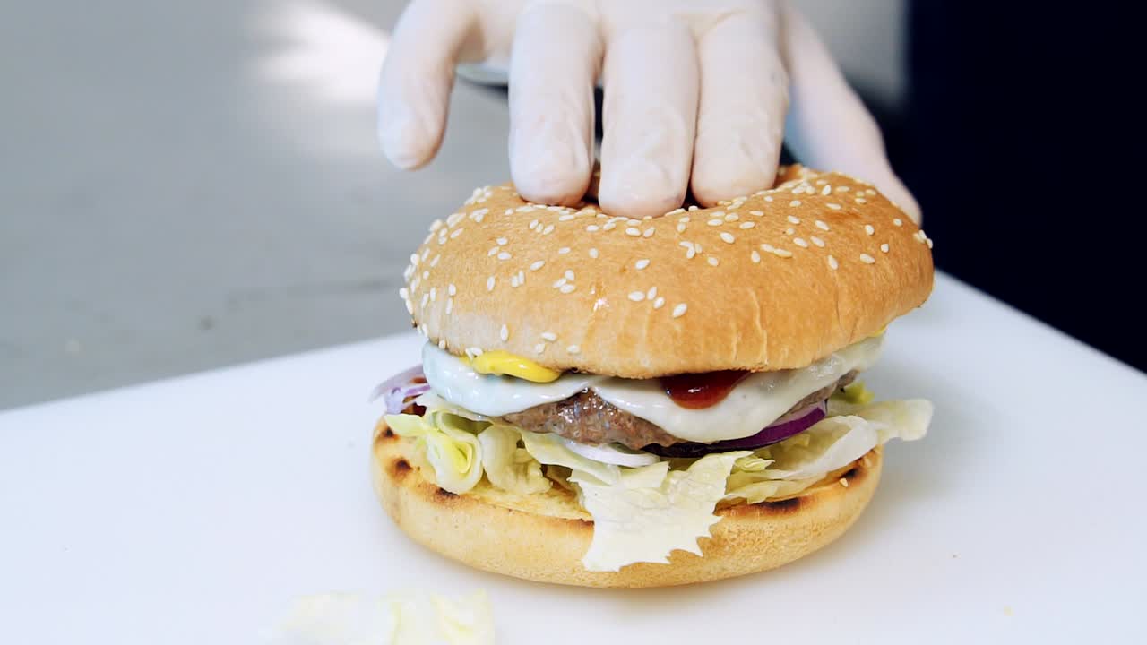 Cook pouring tomato sauce and compounds burger. Preparing delicious burger. Chef cooking burger with meat, cheese and vegetables. Yummy hamburger