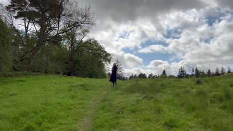 1 girl with black dress walks towards trees green grass near meadow