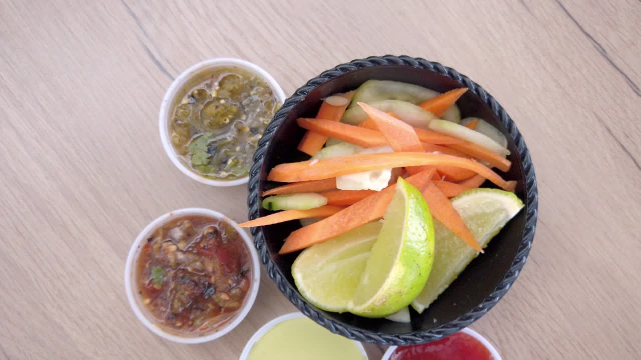 Traditional Mexican food with carrot sticks, lime slices and salsa in black bowl