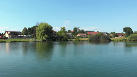 Toma-De-Drones-Del-Lago-Podpeč-En-Eslovenia-Con-Un-Vuelo-Sobre-El-Nivel-Del-Agua-Con-Una-Elevación-Sobre-El-Pueblo