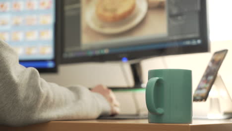 person working at a computer with a hot drink on the desk