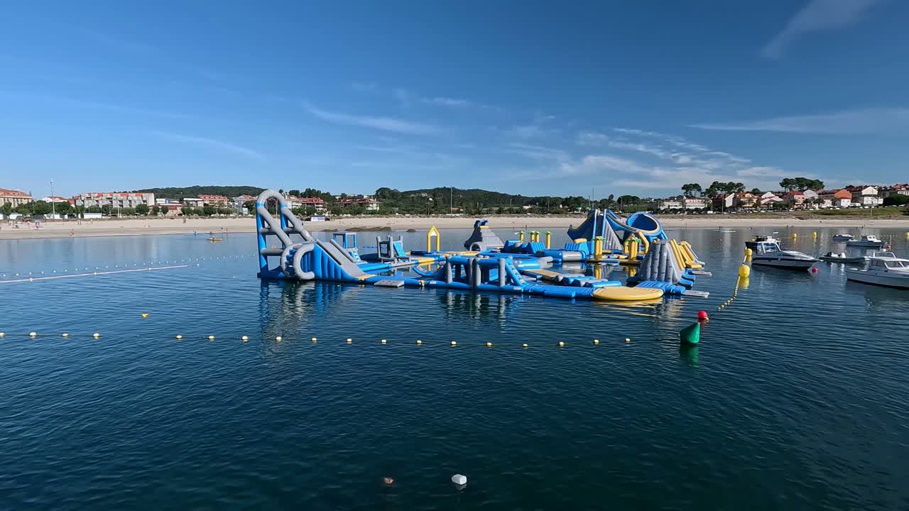 바다 위에 떠다니는 거대한 체육관, 배경에는 관광객들에게 임대되는 해변과 주택 건물, 은 여름 아침, 왼쪽으로 여행하는