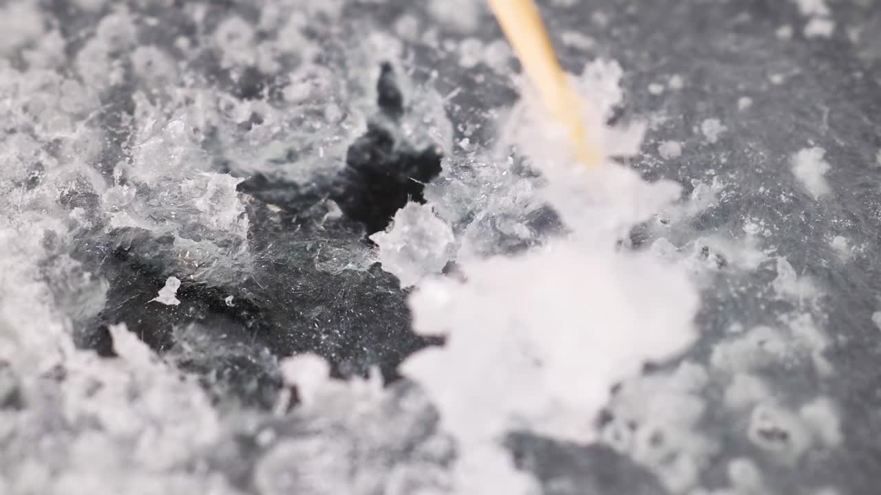 A detailed view of crystal growth as a stick interacts with the surface, highlighting texture and structure.