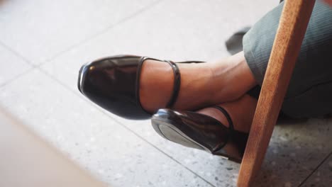 person's feet in dark shiny shoes resting under a chair