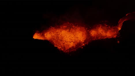 abajo de la parte superior de la lava brillante naranja explotando desde el cráter del volcán por la noche, islandia