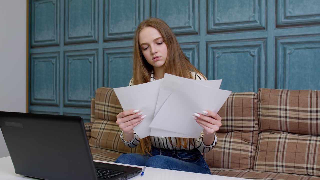 Woman sittingat home looking at documents analyzes data checks papers working on laptop computer