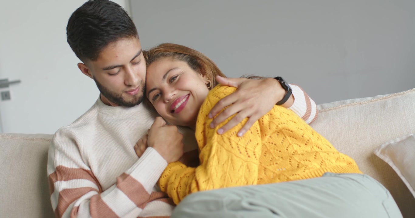 African American couple on sofa at home, woman in yellow leaning on man's chest after smiling