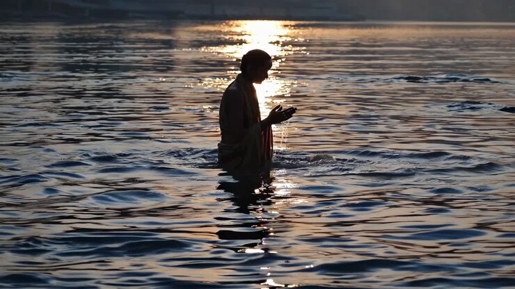 Silhouette of a person praying in a river at sunrise, captured from a low angle