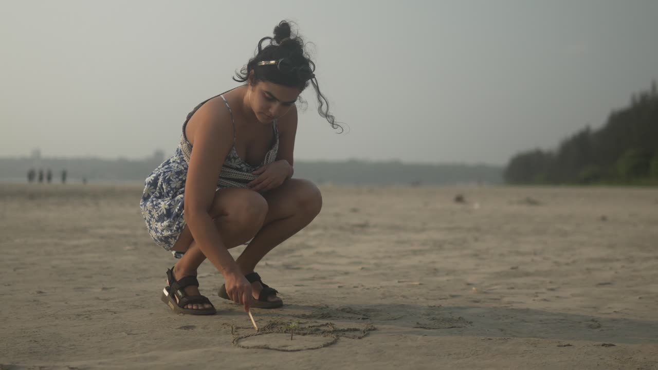 한 여성이 조용한 해변의 모래에 심장을 그립니다.