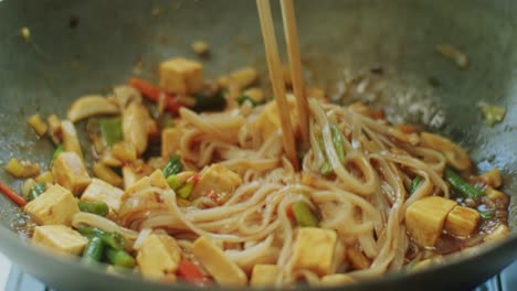 woman mixing delicious wok noodles with chopsticks