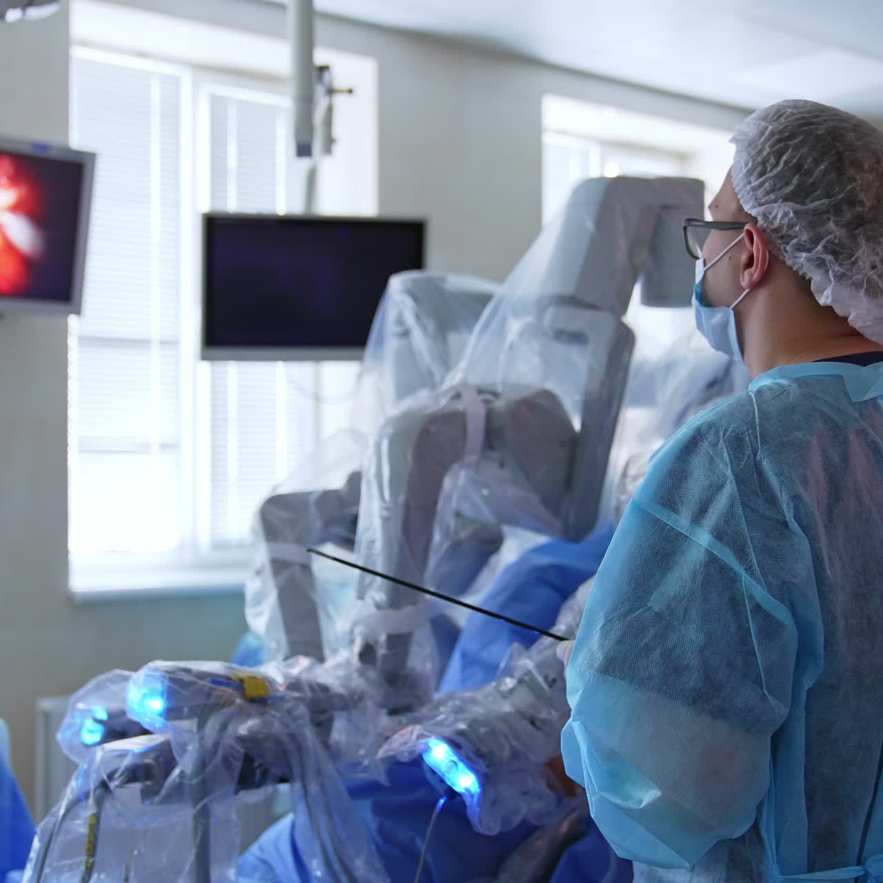 Male surgeon watching the operated area at the screen. Monitor on the wall shows the work of robotic arm in surgery