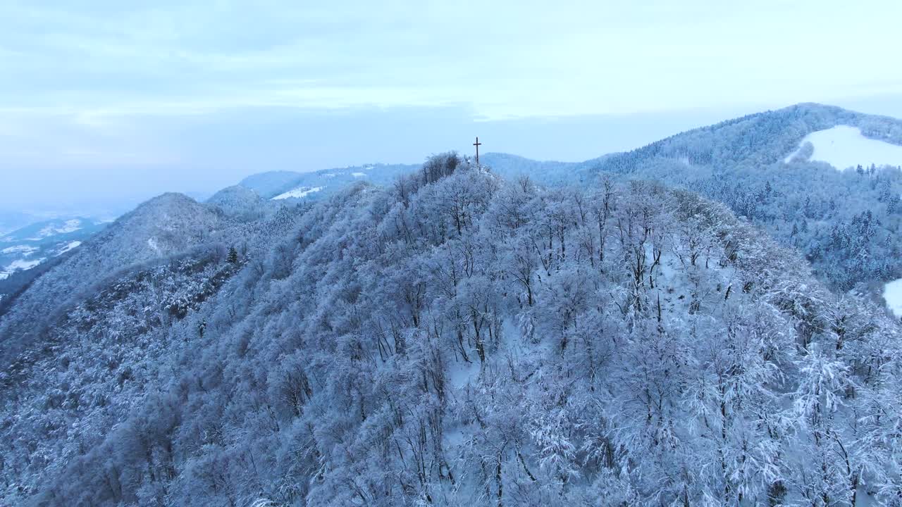 Aerial rotating drone clip of a a mountain peak in Celje-Slovenia revealing a cross structure over the winter snowed mountain area