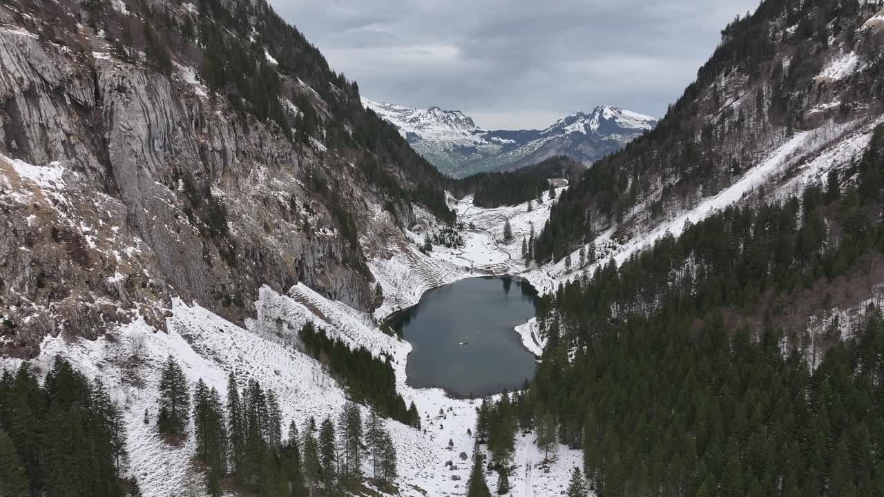 vista aérea de tahlalpsee en filzbach, glarus nord, suiza, rodeado de bosques cubertos de nieve y montañas escarpadas