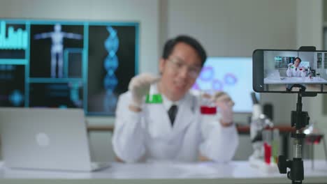 asian scientist man using smartphone recording video while researching in the laboratory, he holding test tube and speaking