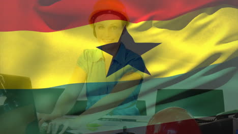 Animación-De-La-Bandera-De-Ghana-Ondeando-Sobre-Una-Mujer-Caucásica-Sonriente-Con-Casco-Trabajando-En-Una-Computadora