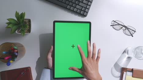 vista de arriba hacia abajo de una computadora portátil con pantalla verde simulada pantalla chromakey en un escritorio de oficina de madera al lado de la libreta con bolígrafos, gafas y un vaso de agua.