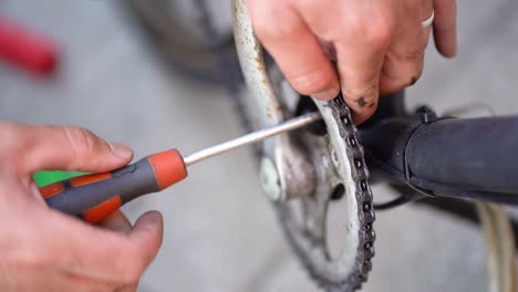 caucasian male mechanic fingers tighten screw on frame of bicycle with screwdriver, above close up static