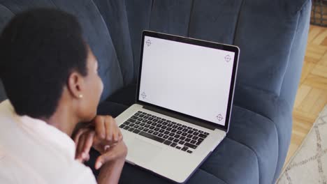 happy african american woman lying on sofa in living room, using laptop with copy space