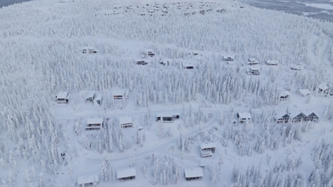 Aerial-tracking-shot-of-mountain-lodges-on-the-side-of-a-fell,-winter-in-Lapland