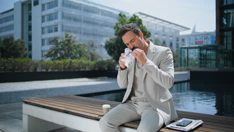 relaxed businessman eating sandwich at wooden bench.  man lunch break