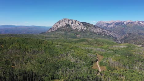 vista aérea lenta de las montañas marcellina cara sur cerca de crested butte colorado durante un claro día de otoño con carretera de tierra debajo