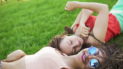 retrato de estilo de vida de verano de dos mujeres hipster acostadas en la hierba, disfrutando de un buen día, con gafas de sol brillantes. mejores amigas