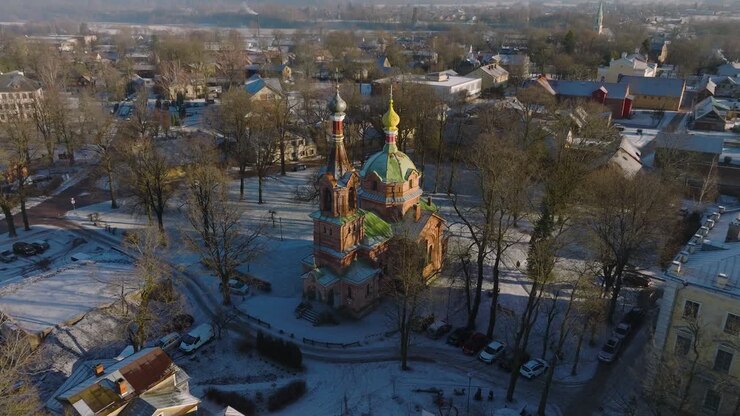 Aerial establishing view of Kuldiga Old Town , houses with red roof tiles, orthodox church, sunny winter day, travel destination, wide drone shot moving forward, tilt down