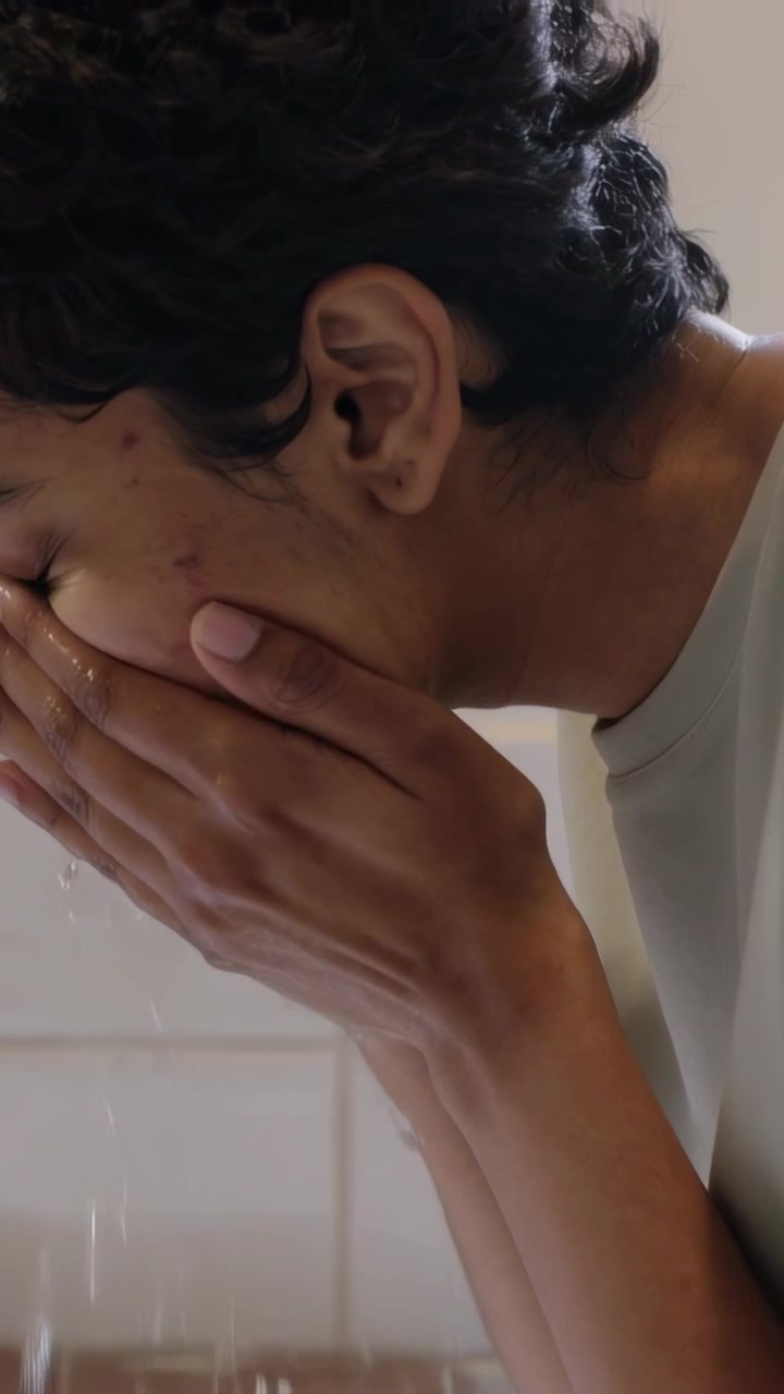 Vertical video: Running faucet making woman in tee cupping water splashing washing face at sink