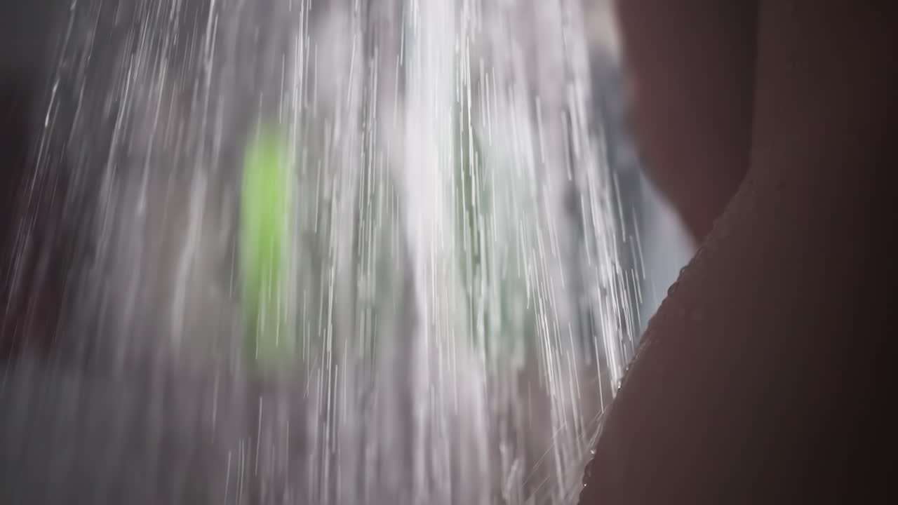 Naked woman washes under flow of water in shower. Bare woman stands enjoying refreshing shower. Nude woman stands under cascade of water in shower