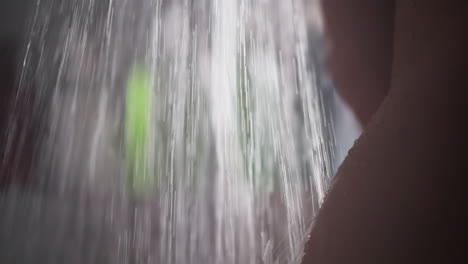 naked woman washes under flow of water in shower. bare woman stands enjoying refreshing shower. nude woman stands under cascade of water in shower