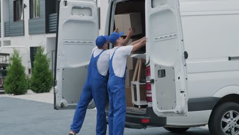 dos jóvenes trabajadores de una compañía de mudanzas están cargando cajas y muebles en un minibus