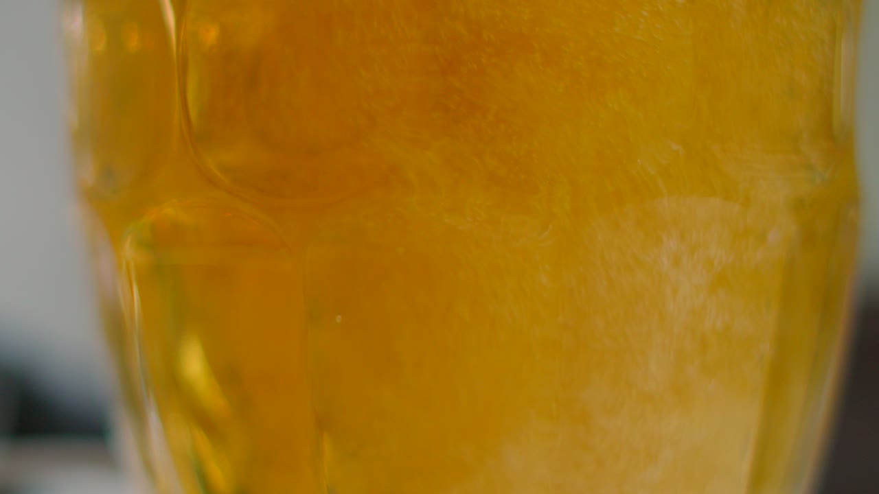 Slow Motion Shot of Beer Being Poured into Glass in Slow Motion with Hundreds of Bubbles Swirling and Rising. Freshly Chilled Alcoholic Beverage